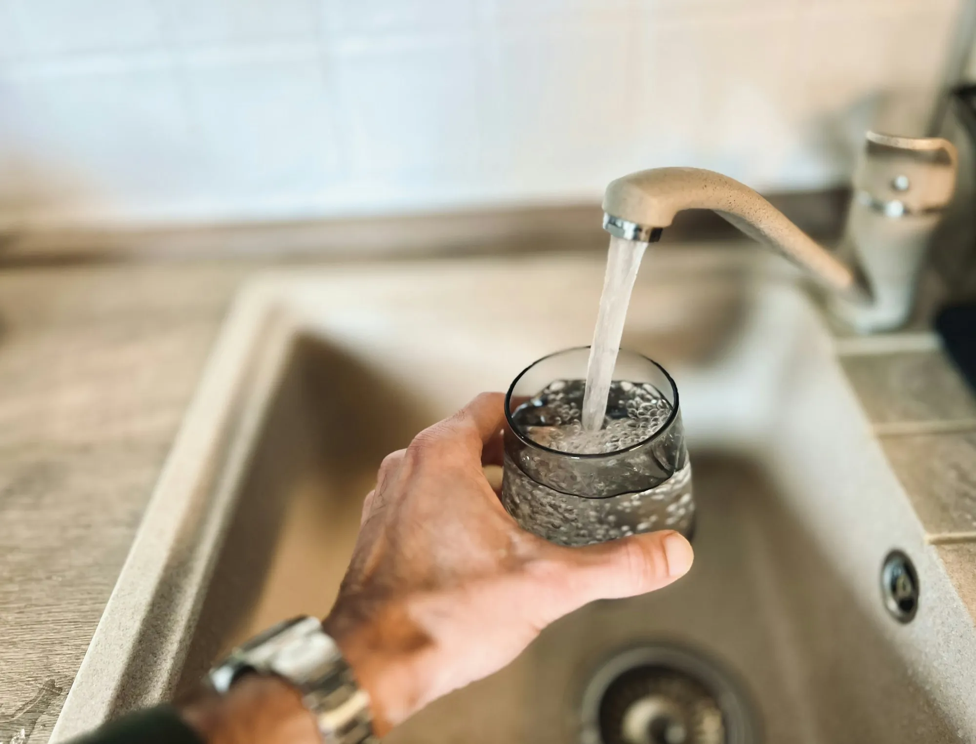 Hand filling a glass of water at a kitchen sink